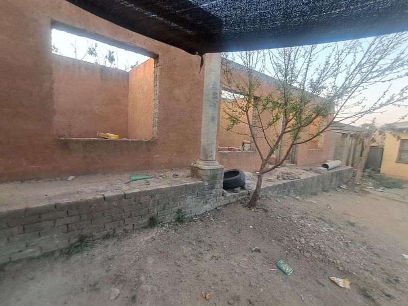 An unfinished exterior rear structure featuring exposed masonry walls, a stone column, and open window apertures, requiring significant completion and renovation.