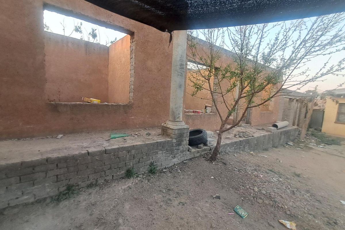 An unfinished exterior rear structure featuring exposed masonry walls, a stone column, and open window apertures, requiring significant completion and renovation.
