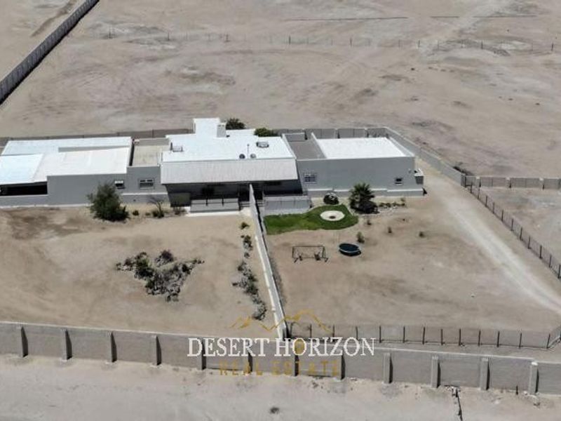 Aerial view of a property on a large plot, featuring a main dwelling, perimeter wall, and expansive surrounding land.