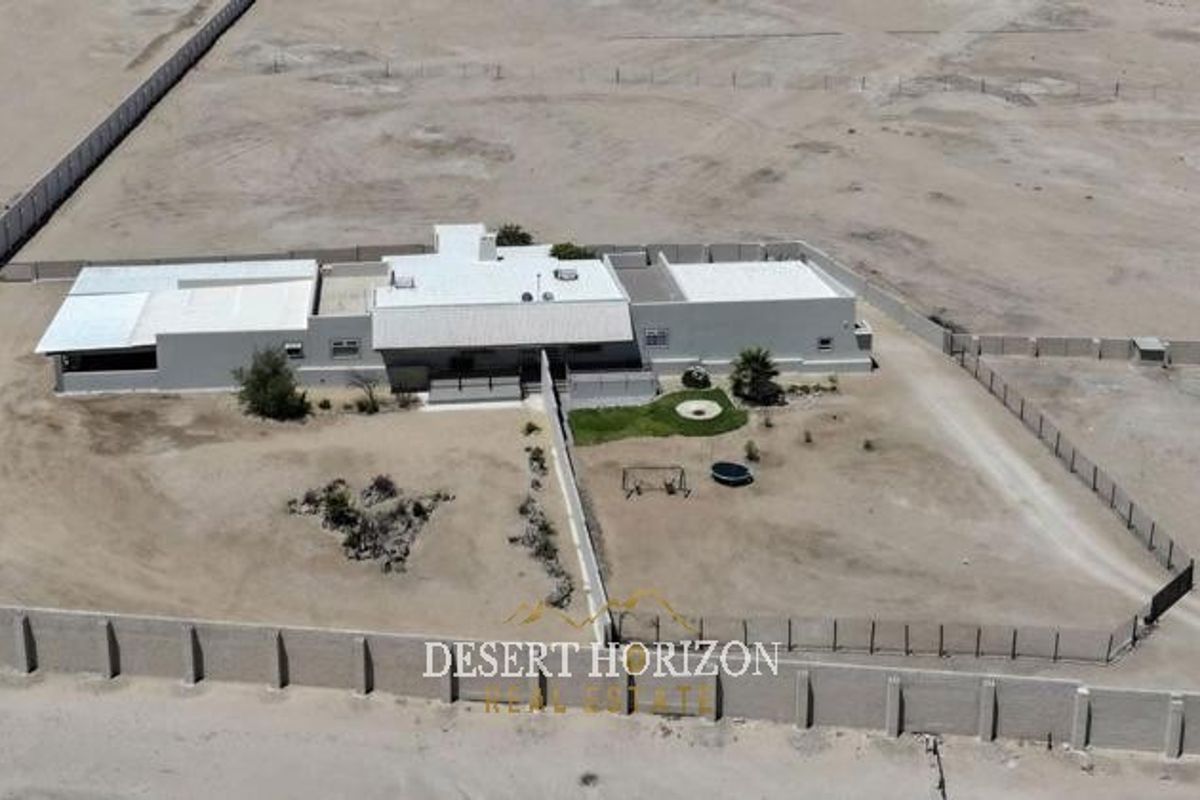 Aerial view of a property on a large plot, featuring a main dwelling, perimeter wall, and expansive surrounding land.
