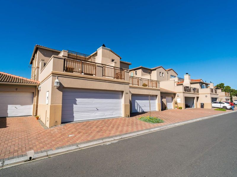 Street view of a townhouse complex featuring multiple garage doors, paved driveways, and upper-level balconies with metal railings.