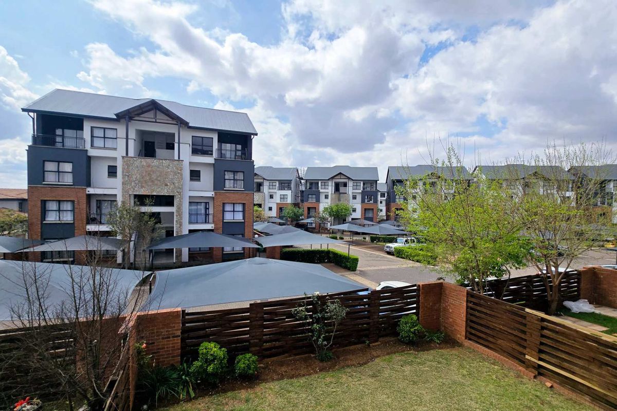 Elevated view of the apartment complex grounds featuring landscaped garden areas, brick boundary walls, and covered parking bays.