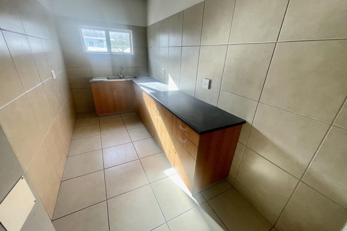A functional office kitchenette featuring tiled walls, laminate cabinetry, a dark countertop, and a stainless steel sink.
