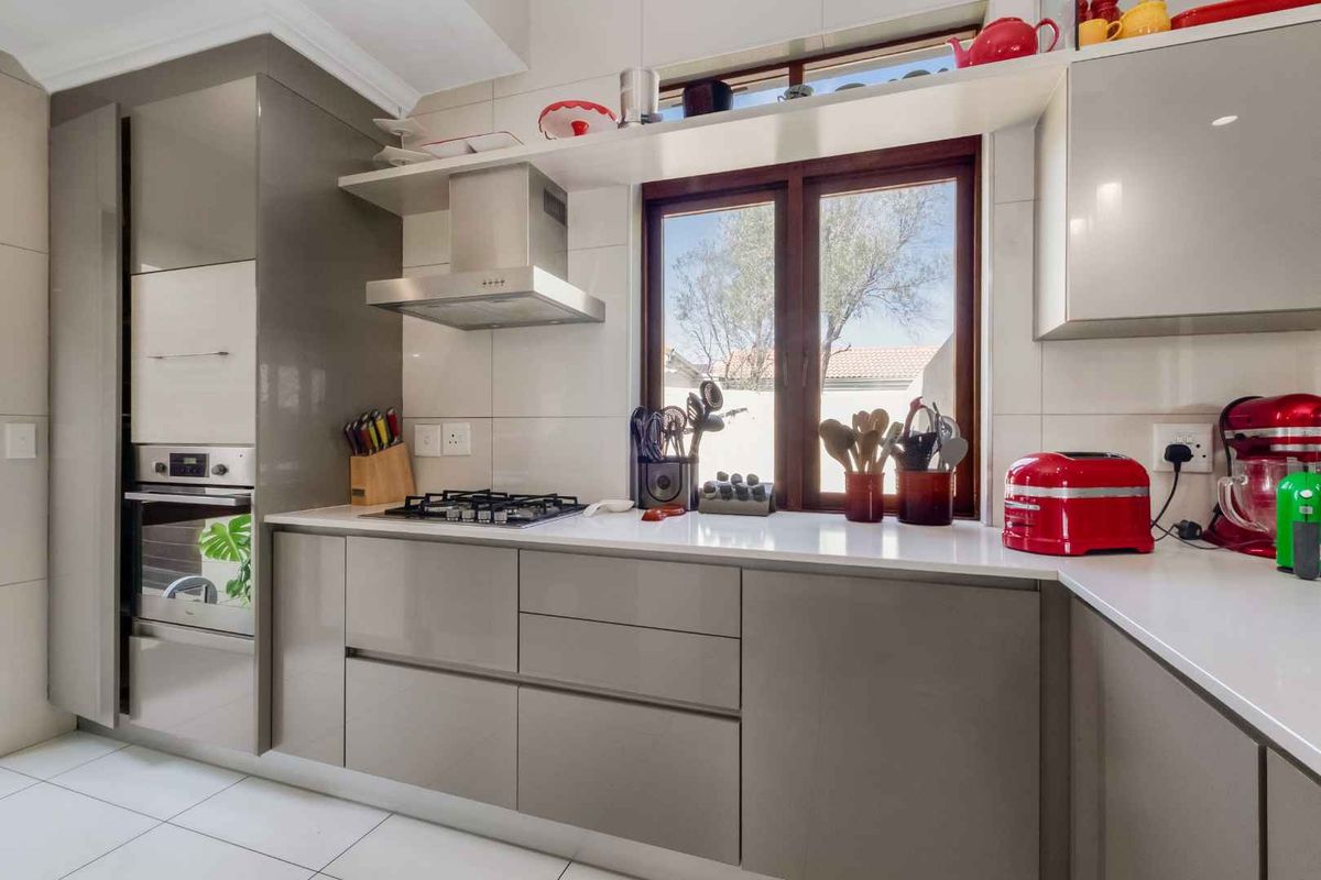 Modern kitchen featuring sleek gloss cabinetry, quartz countertops, built-in oven, gas hob, and stainless steel extractor fan with a tiled backsplash.