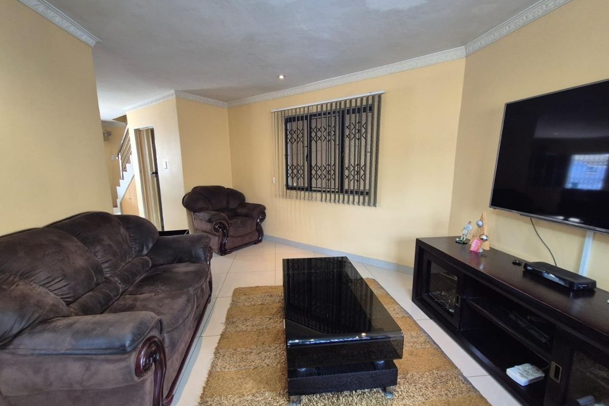 A living room featuring tiled floors, crown molding, and a security gate on the window. Visible water staining on the ceiling requires attention.