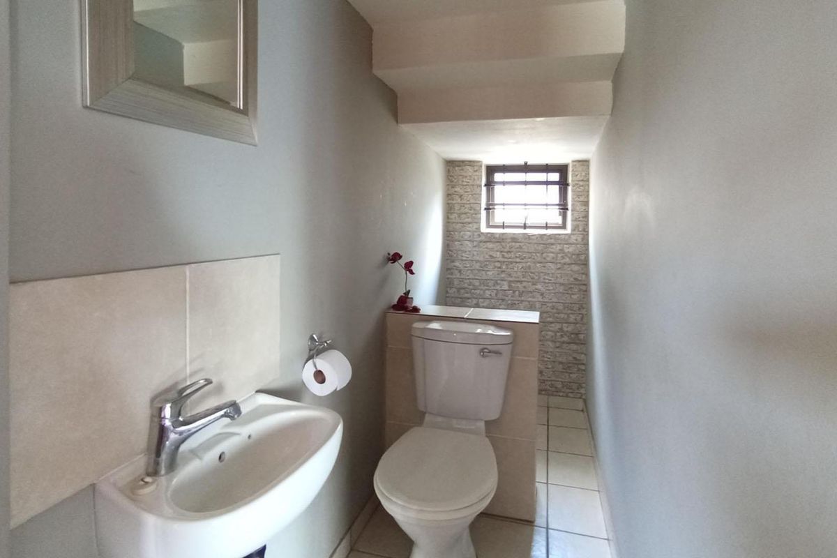 A compact guest bathroom featuring a wall-mounted basin, a standard toilet, and a small window with security bars.