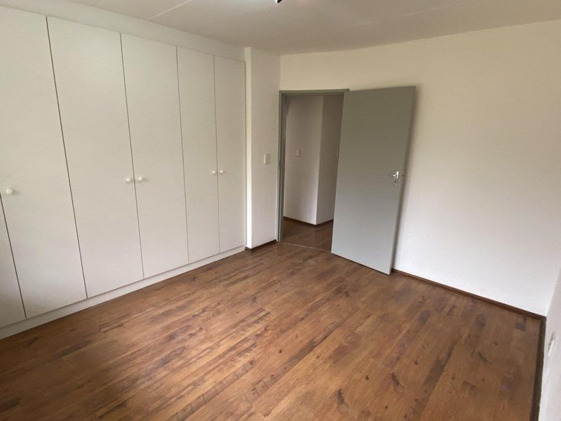 A clean, empty bedroom featuring laminate flooring and extensive built-in cupboard storage, offering a neutral canvas for personalization.
