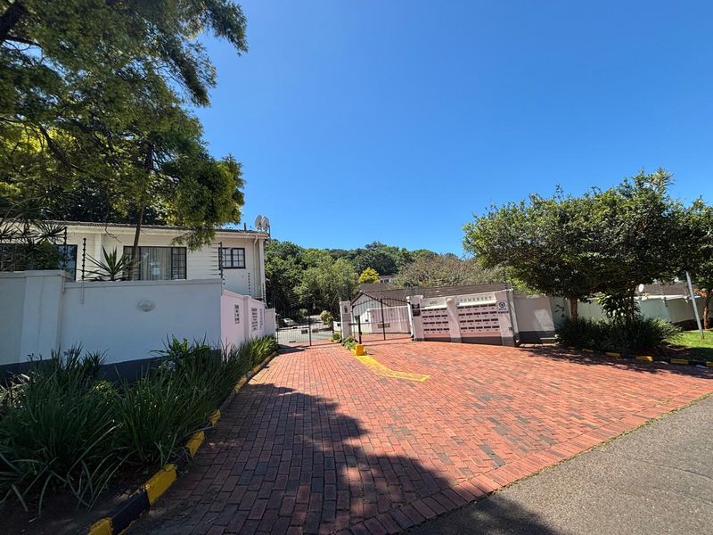 Front entrance view of the apartment complex featuring a brick paved driveway, secure gated access, and a bank of post boxes.