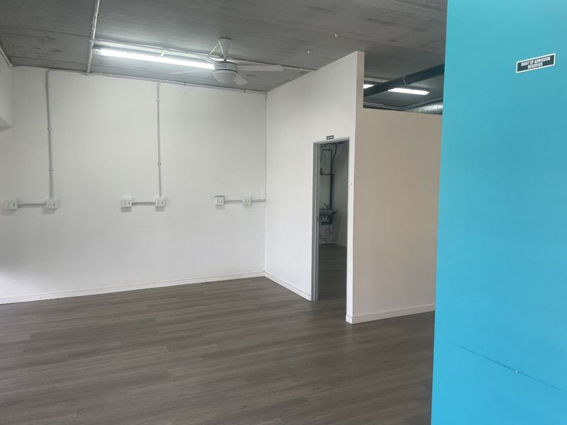 An open-plan retail space featuring laminate flooring, exposed ceilings, surface-mounted electrical conduits, and a separate utility area.