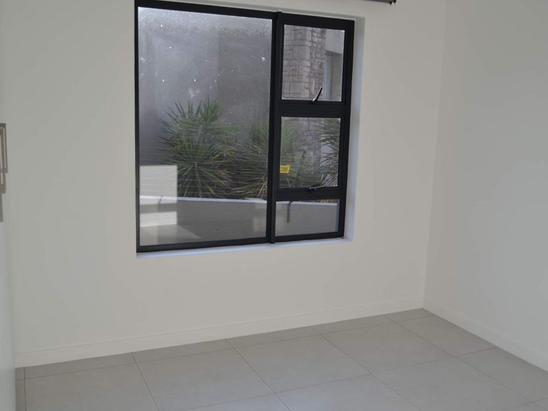 A clean, empty bedroom featuring neutral tiled flooring, white walls, and a modern black-framed window.