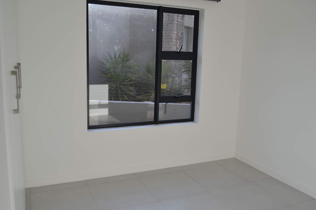 A clean, empty bedroom featuring neutral tiled flooring, white walls, and a modern black-framed window.