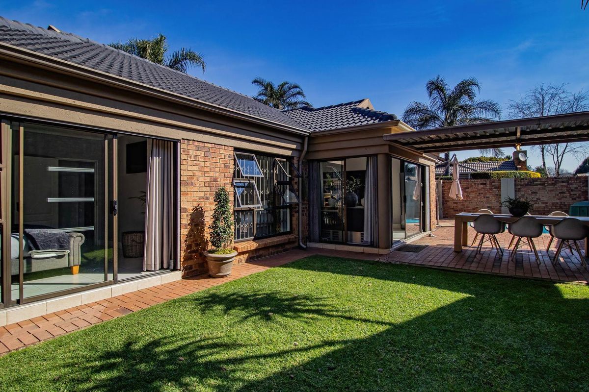 A well-maintained rear exterior featuring a brick facade, paved patio area with a covered pergola, and direct access to the garden via sliding doors.