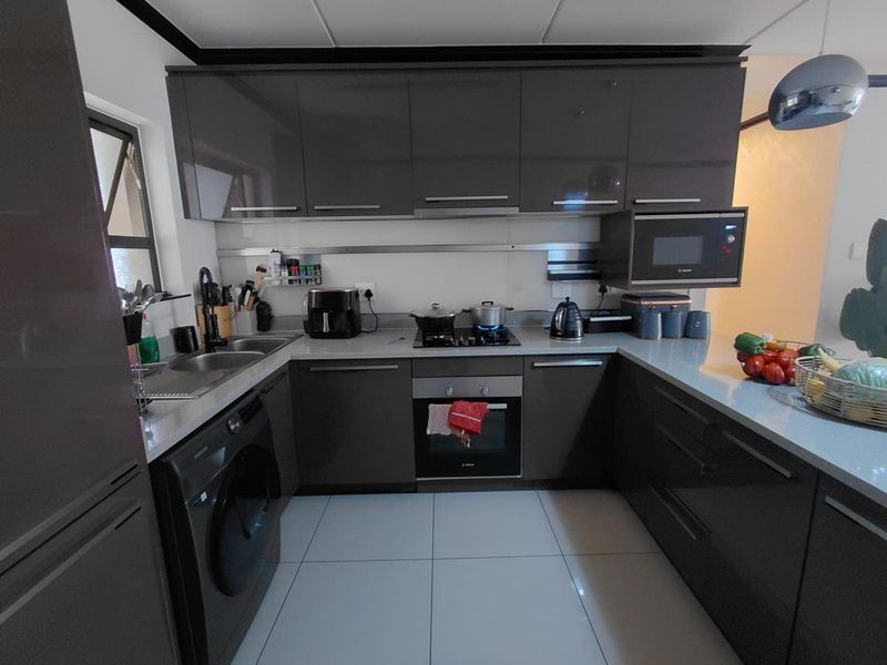 Modern kitchen featuring dark grey high-gloss cabinetry, stone countertops, integrated appliances, and tiled flooring in a functional U-shaped layout.