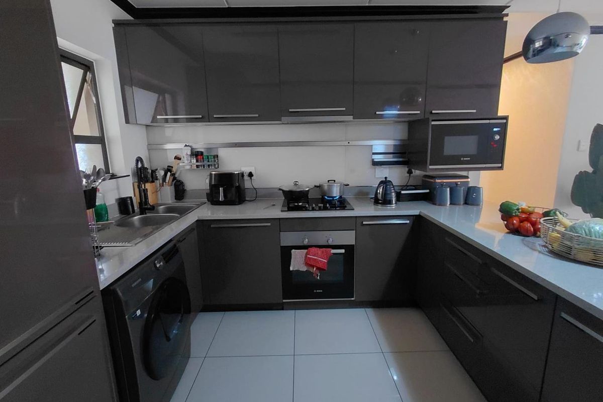 Modern kitchen featuring dark grey high-gloss cabinetry, stone countertops, integrated appliances, and tiled flooring in a functional U-shaped layout.