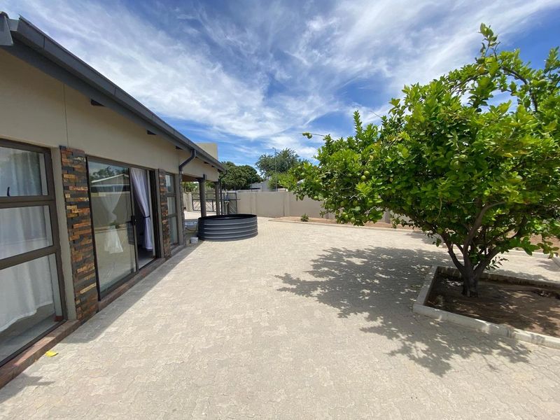 A well-maintained rear exterior featuring a paved patio area, stone-clad accents, sliding glass doors, and a boundary wall.