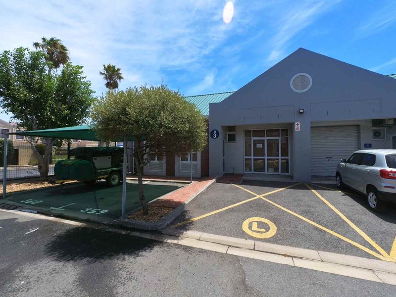 Front exterior view of the office unit featuring a paved parking area, shaded bay, and a combination of roller shutter and glass entrance doors.