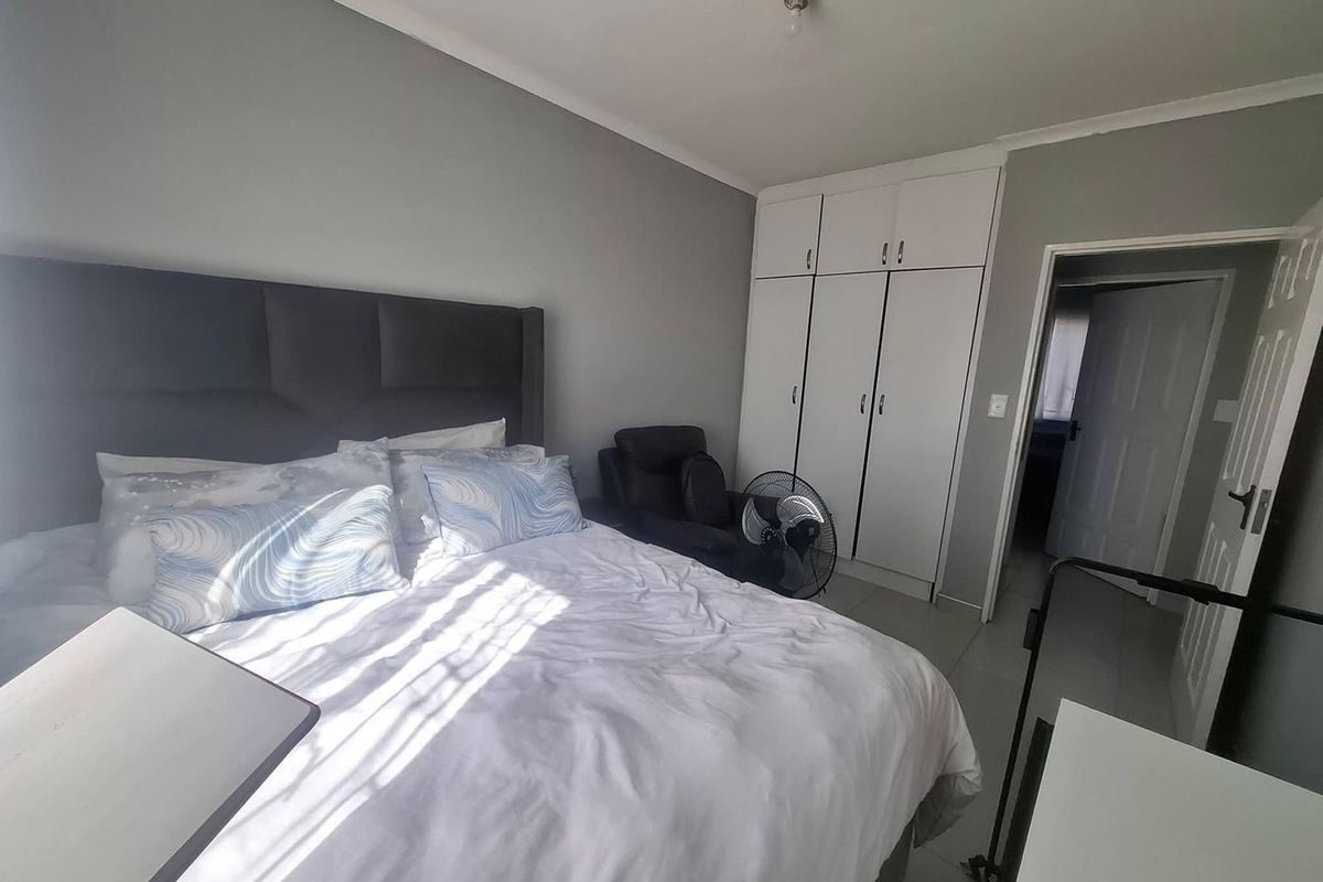 A functional bedroom featuring built-in cupboards, neutral grey walls, and tiled flooring, offering a clean and practical living space.