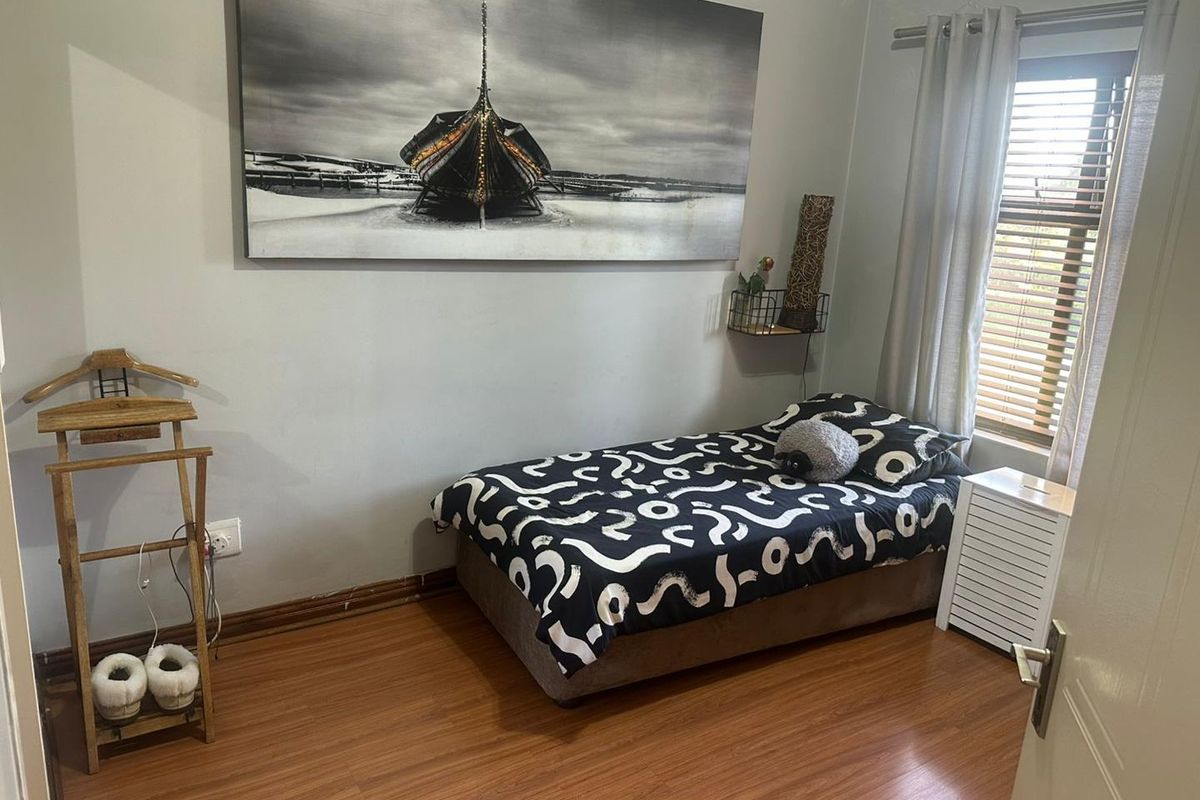 A compact bedroom featuring laminate wood flooring, a window with fitted blinds, and neutral wall finishes.