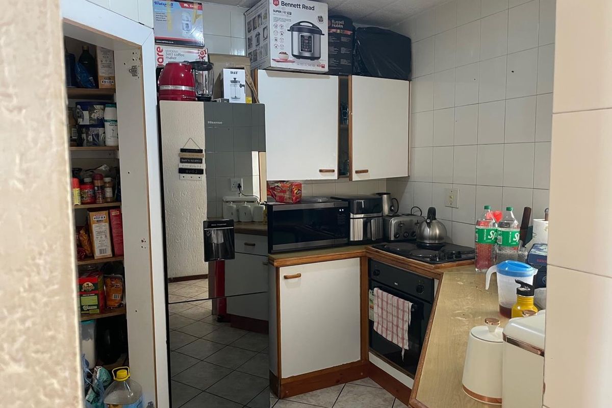 Compact kitchen featuring built-in cabinetry, oven, hob, and a dedicated pantry cupboard with tiled splashbacks and flooring.