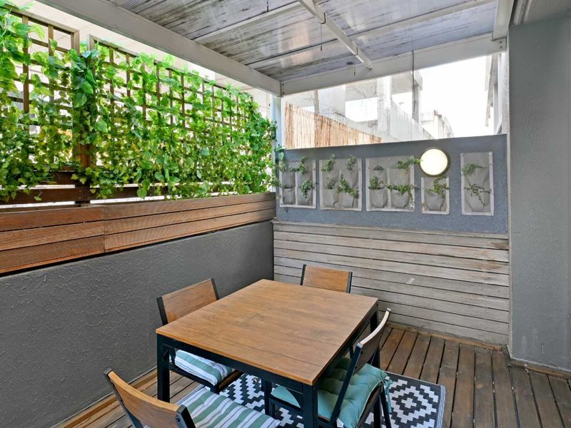 A covered balcony featuring timber decking, a privacy screen with integrated trellis, and wall-mounted lighting, providing a functional outdoor entertainment space.