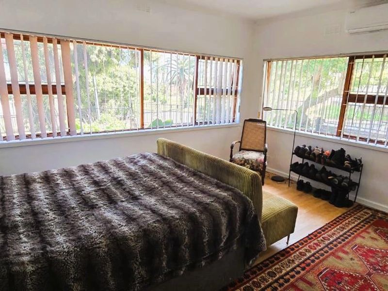 A bright bedroom featuring large windows with vertical blinds, timber flooring, and a wall-mounted split-system air conditioner.