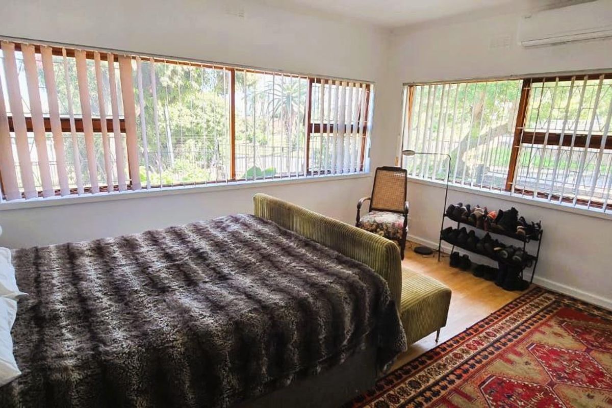 A bright bedroom featuring large windows with vertical blinds, timber flooring, and a wall-mounted split-system air conditioner.