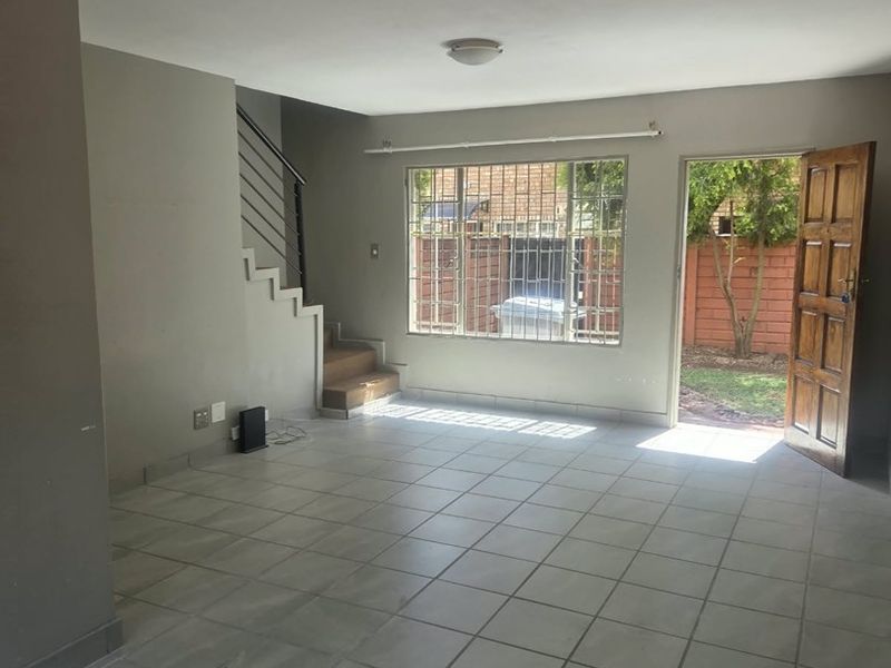 An open-plan living area featuring tiled flooring, a staircase with metal railings, and direct access to the rear garden through a timber door.