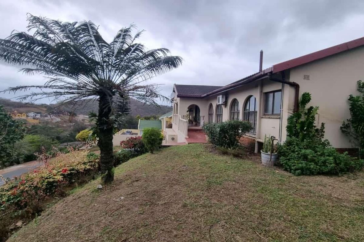 Rear view of the property featuring arched windows, a tiled roof, and a concrete patio area overlooking the surrounding landscape.