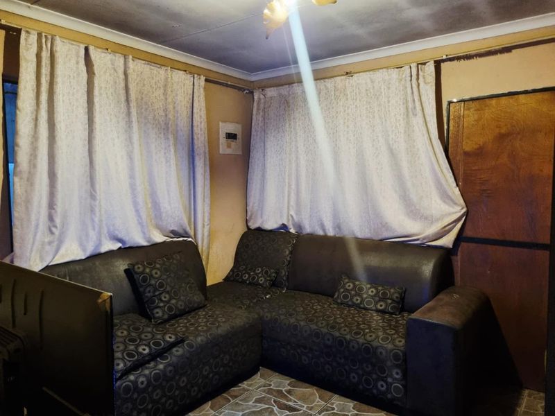 A living room area featuring tiled flooring and an exposed electrical distribution board, showing signs of significant wear and ceiling staining.
