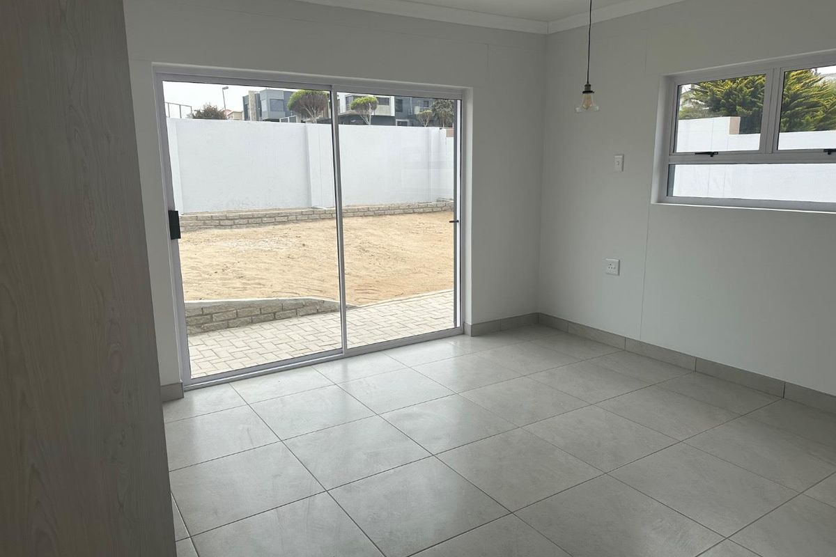 A bright, empty living area featuring large sliding glass doors that open onto a paved patio and garden space.