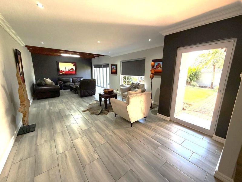 Spacious living room featuring modern wood-look tiled flooring, recessed downlights, exposed timber ceiling beams, and large glass sliding doors providing access to the garden.