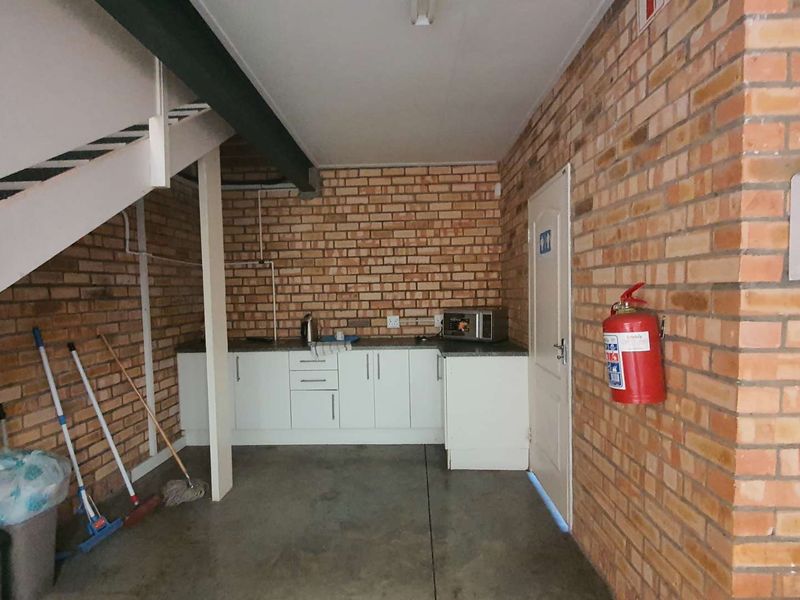 A utility space featuring exposed brick walls, built-in cabinetry with a sink, a staircase, and a wall-mounted air conditioning unit.