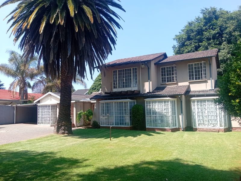 A well-maintained double-story residential property featuring a paved driveway, expansive lawn, and distinctive bay windows under a tiled roof.
