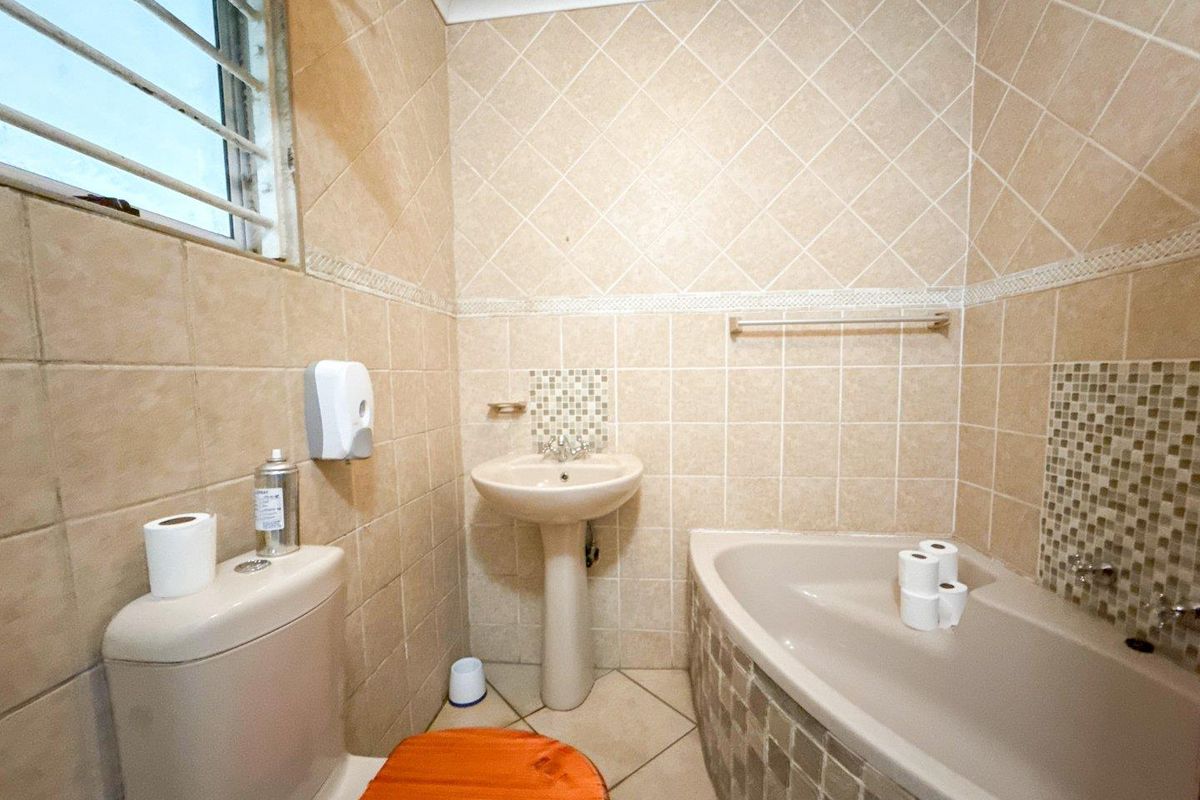 Compact bathroom featuring a corner bathtub, pedestal basin, and neutral ceramic tiling throughout.