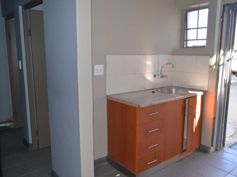 A compact scullery or utility area featuring built-in cabinetry, a stainless steel sink, tiled backsplash, and direct access to the exterior.