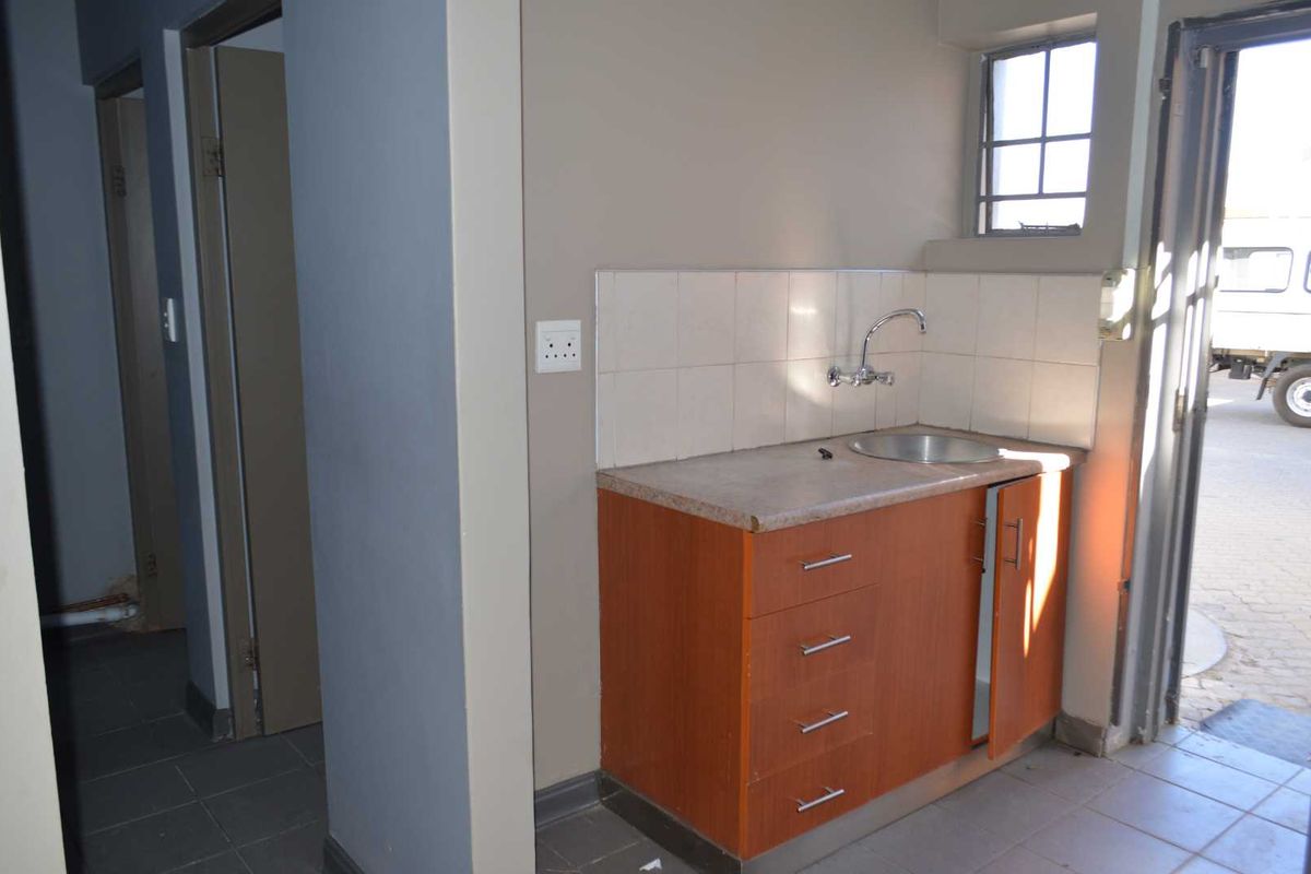 A compact scullery or utility area featuring built-in cabinetry, a stainless steel sink, tiled backsplash, and direct access to the exterior.