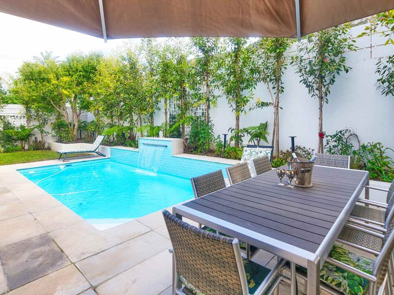 A well-maintained outdoor pool area featuring a built-in water feature, stone paving, and landscaped garden borders.