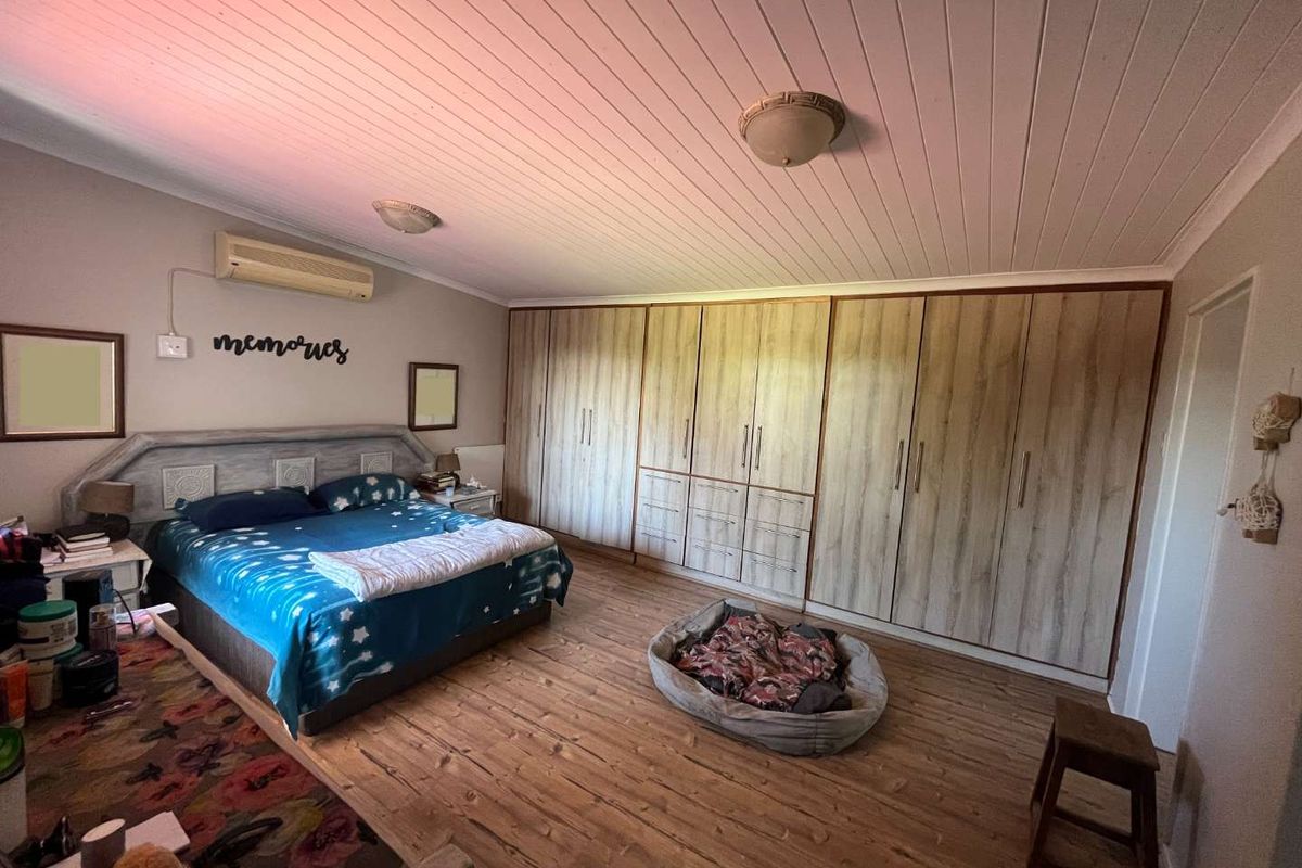 Spacious bedroom featuring extensive built-in wooden cabinetry, timber-look flooring, a white panelled ceiling, and a wall-mounted air conditioning unit.