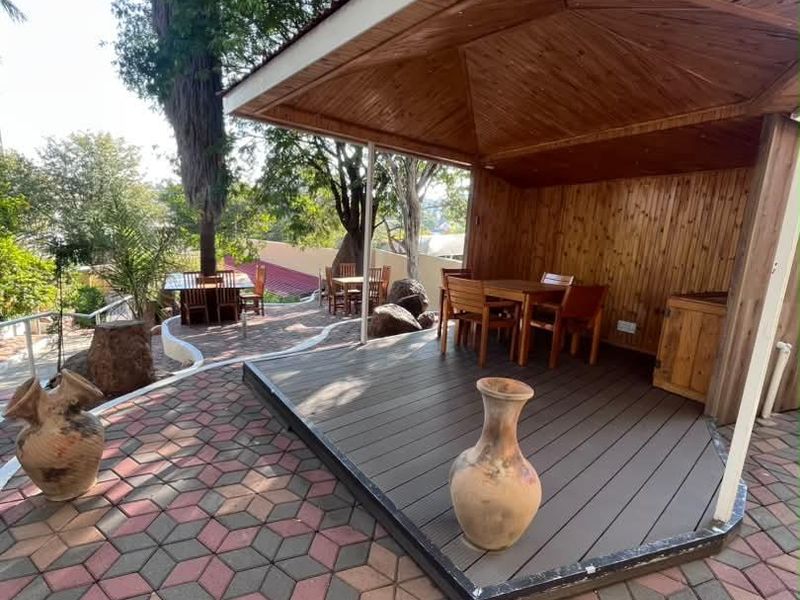 A covered outdoor timber gazebo with decking, set within a landscaped garden area featuring paved walkways and mature trees.