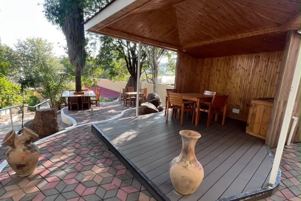 A covered outdoor timber gazebo with decking, set within a landscaped garden area featuring paved walkways and mature trees.
