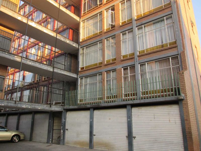 Exterior view of a multi-story apartment building featuring brick facade, ground-level roller garage doors, and external metal walkways.