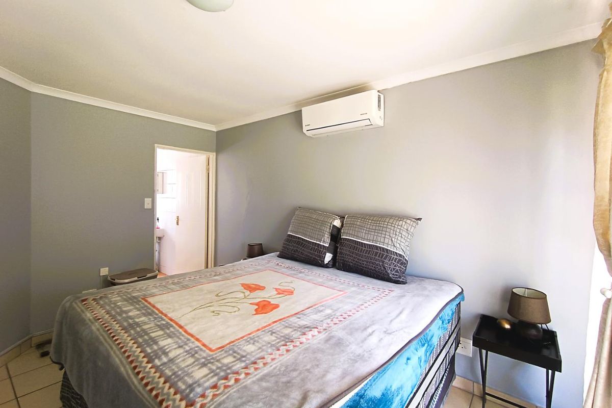 A bedroom featuring tiled flooring, a wall-mounted air conditioning unit, and an adjoining en-suite bathroom.