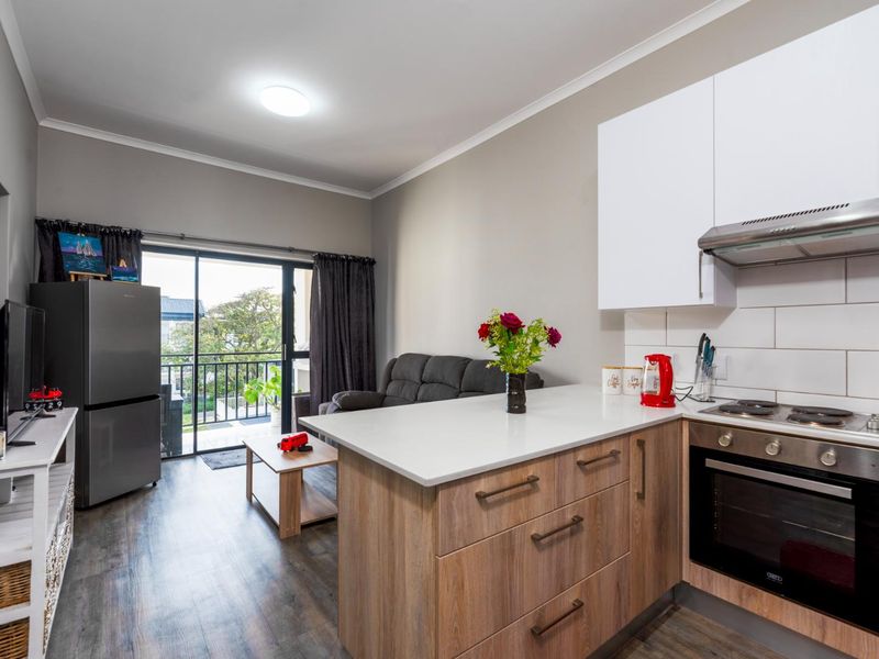 Modern open-plan apartment featuring a well-appointed kitchen with stone countertops and integrated appliances, flowing seamlessly into a living area with balcony access.