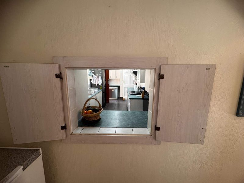 A kitchen serving hatch with wooden shutters providing a view into the main kitchen area with laminate countertops and cabinetry.