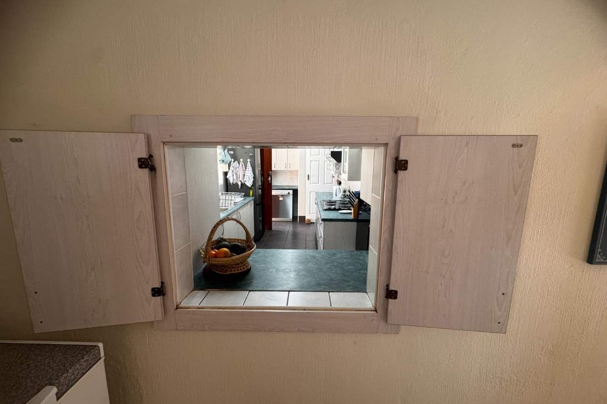 A kitchen serving hatch with wooden shutters providing a view into the main kitchen area with laminate countertops and cabinetry.