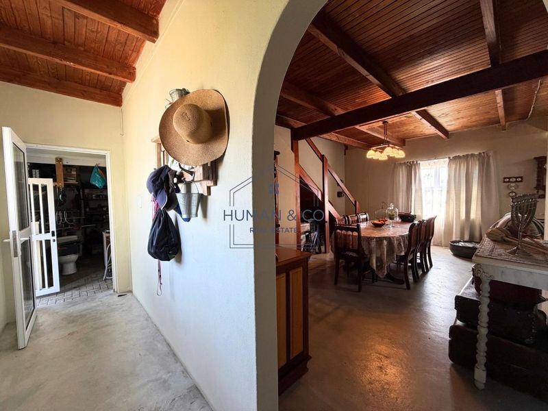 Open plan living and dining area featuring exposed timber ceiling beams, concrete flooring, and an arched transition to an adjacent utility space.