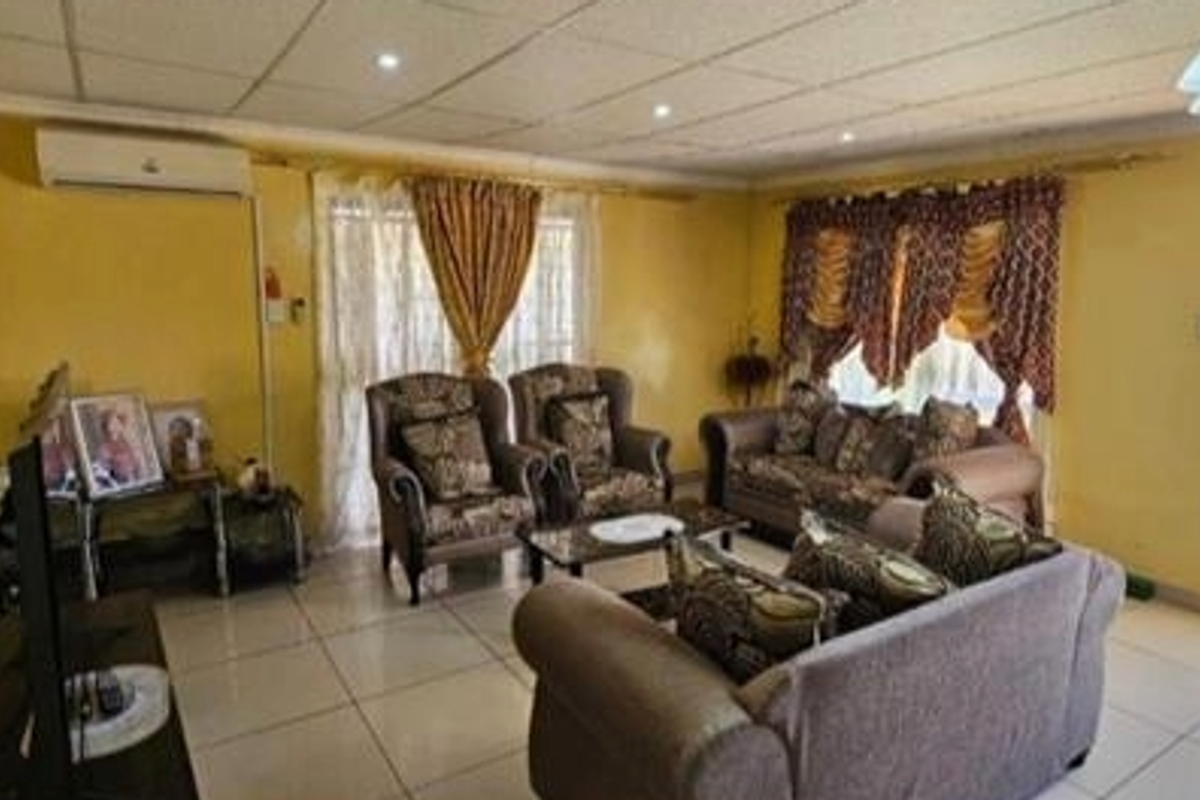 A spacious living room featuring tiled flooring, a split-system air conditioner, and direct access to the outdoor area through a glass panel door.