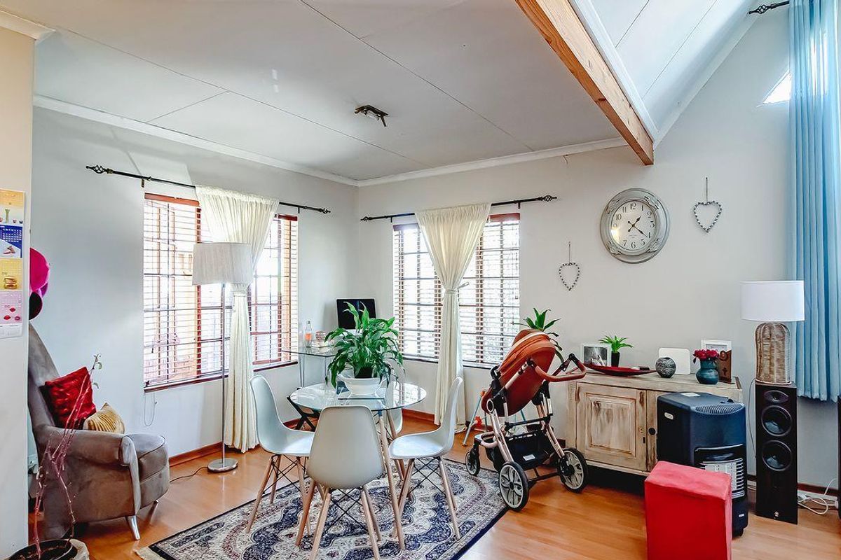 A bright living area featuring high vaulted ceilings with exposed timber beams, large windows with blinds, and laminate wood flooring.