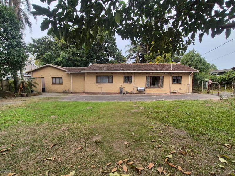 Rear view of a single-story residential property featuring a tiled roof, security bars on windows, and a large backyard with a paved driveway area.
