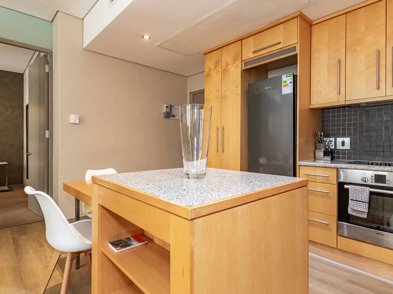 A functional kitchen featuring light wood cabinetry, granite countertops, a built-in oven, and a tiled backsplash, with an integrated island and laminate flooring.